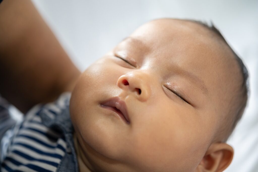 a baby boy in a striped shirt is sleeping in bed.