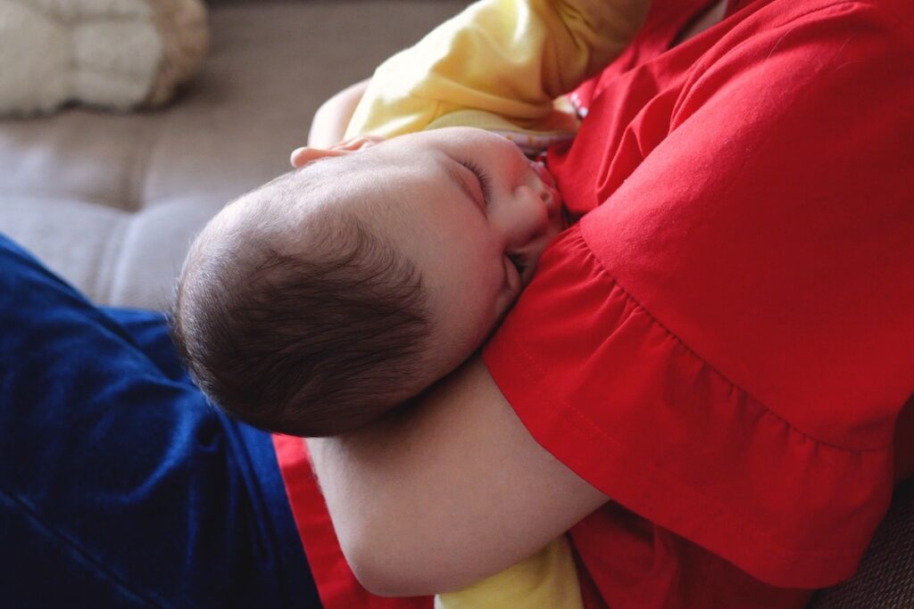 mother breastfeeding baby at home. motherhood and maternity care concept. cheerful mom enjoy breastfeeding